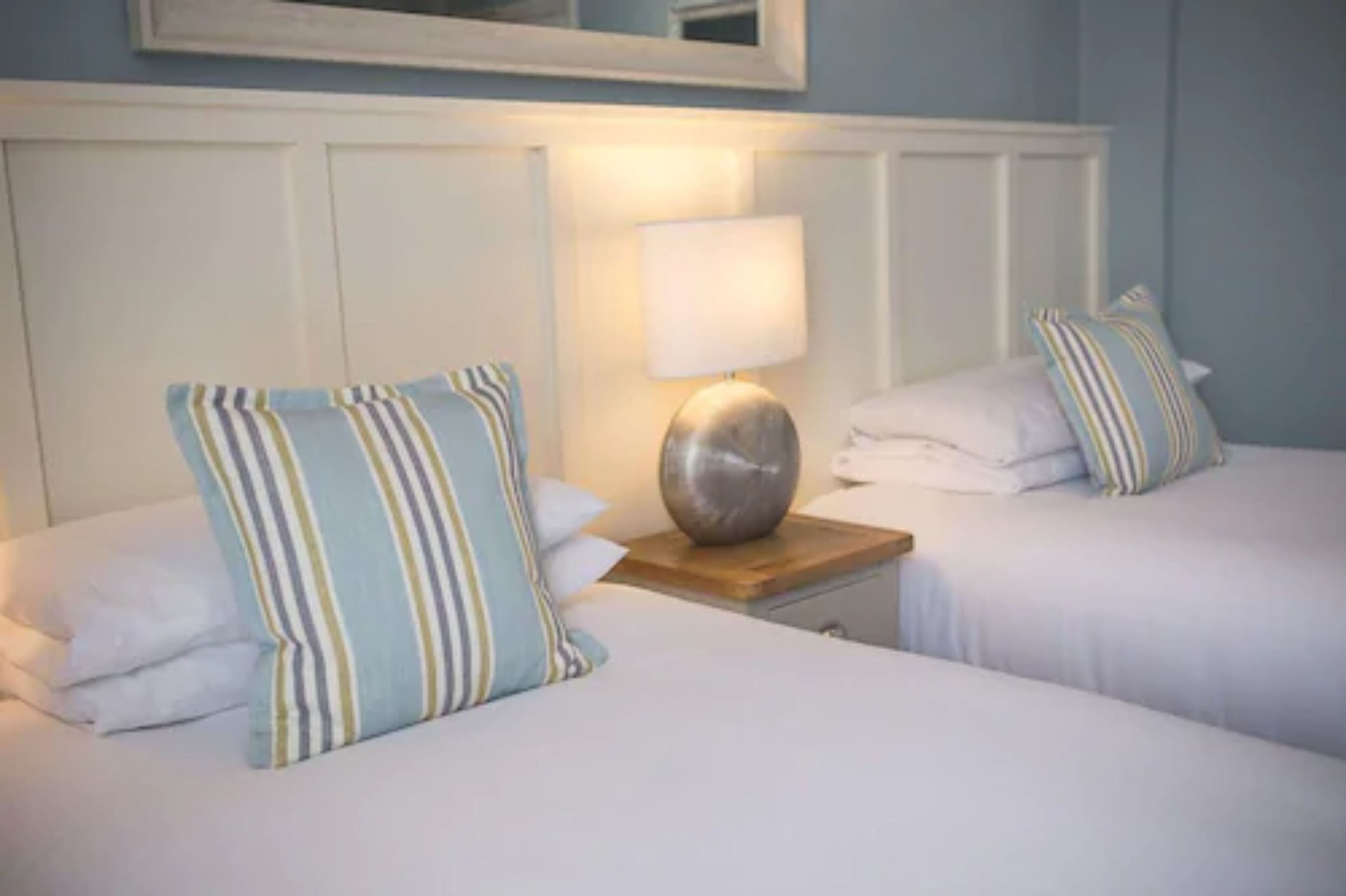 Ein Hotelzimmer mit zwei Betten, einem Nachttisch mit Lampe und einem Spiegel über dem Bett.