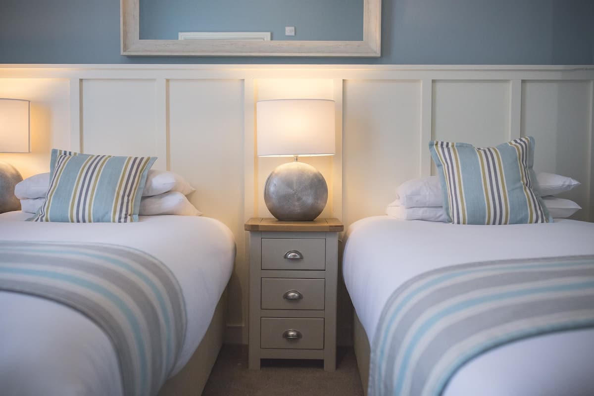 Une chambre d’hôtel avec deux lits, chacun doté de draps et d’oreillers à rayures, une table de chevet avec une lampe et un miroir au-dessus du lit.