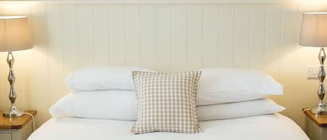 Una cama bien hecha con sábanas blancas y un cojín a cuadros, flanqueada por dos lámparas de noche en mesitas de madera. Una decoración con forma de estrella cuelga sobre la cama.