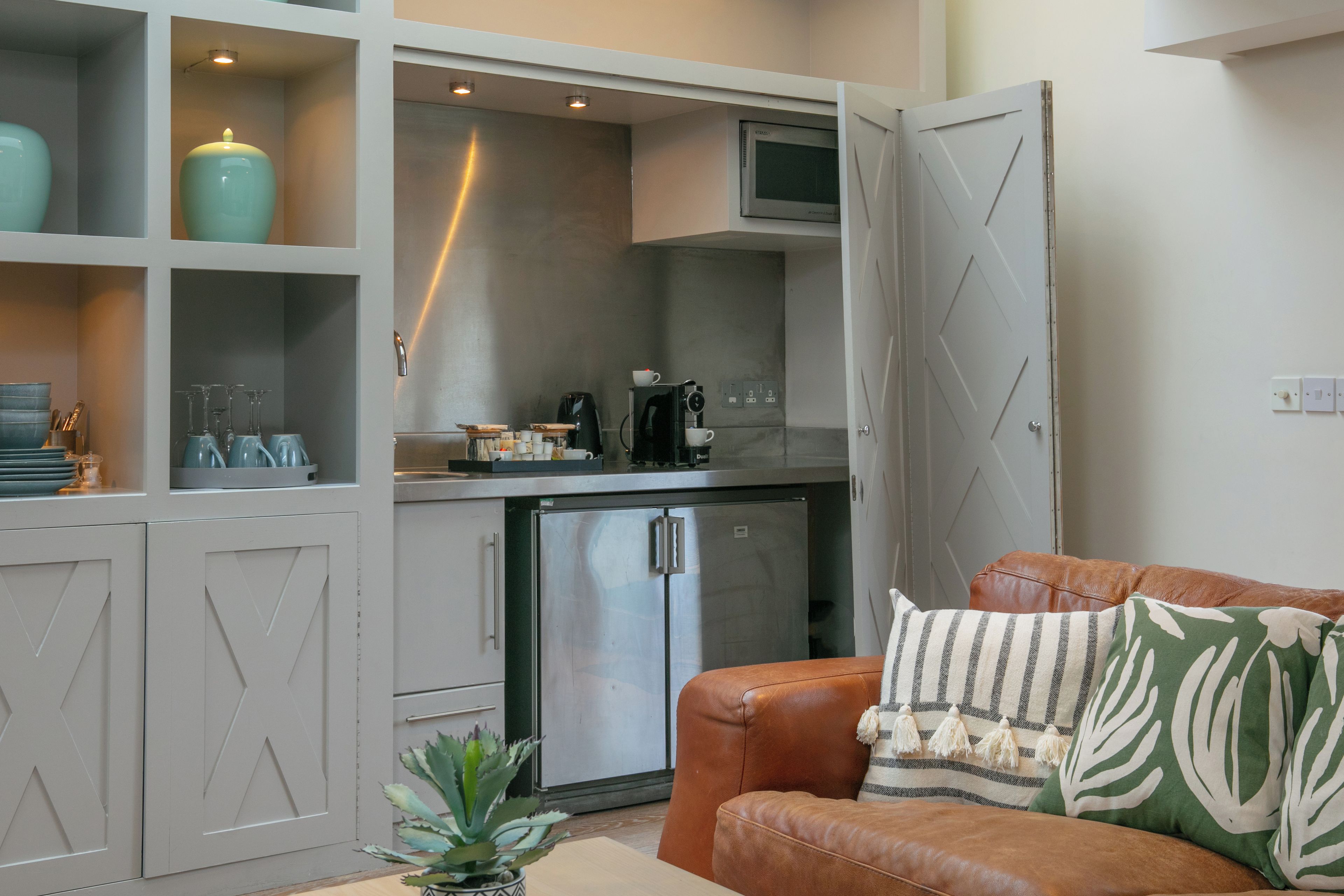 A compact living space with a kitchenette, a refrigerator, and a seating area with a leather couch.