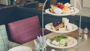 Un service à thé à trois niveaux comprenant des sandwichs, des scones et une fraise. Sur la table, on trouve deux tasses de thé, une théière et un petit vase avec des fleurs.