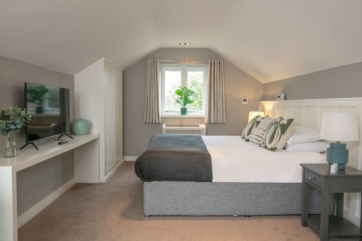 Une chambre à coucher avec un lit, une télévision, un bureau et une fenêtre avec des rideaux.