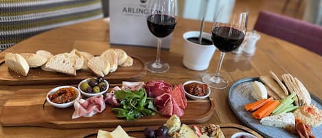 A wooden table with a variety of cheeses, meats, and bread, accompanied by wine glasses and a menu.