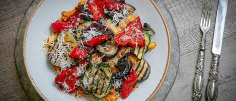 Een bord pasta met gegrilde groenten en kaas, geserveerd op een rond bord.