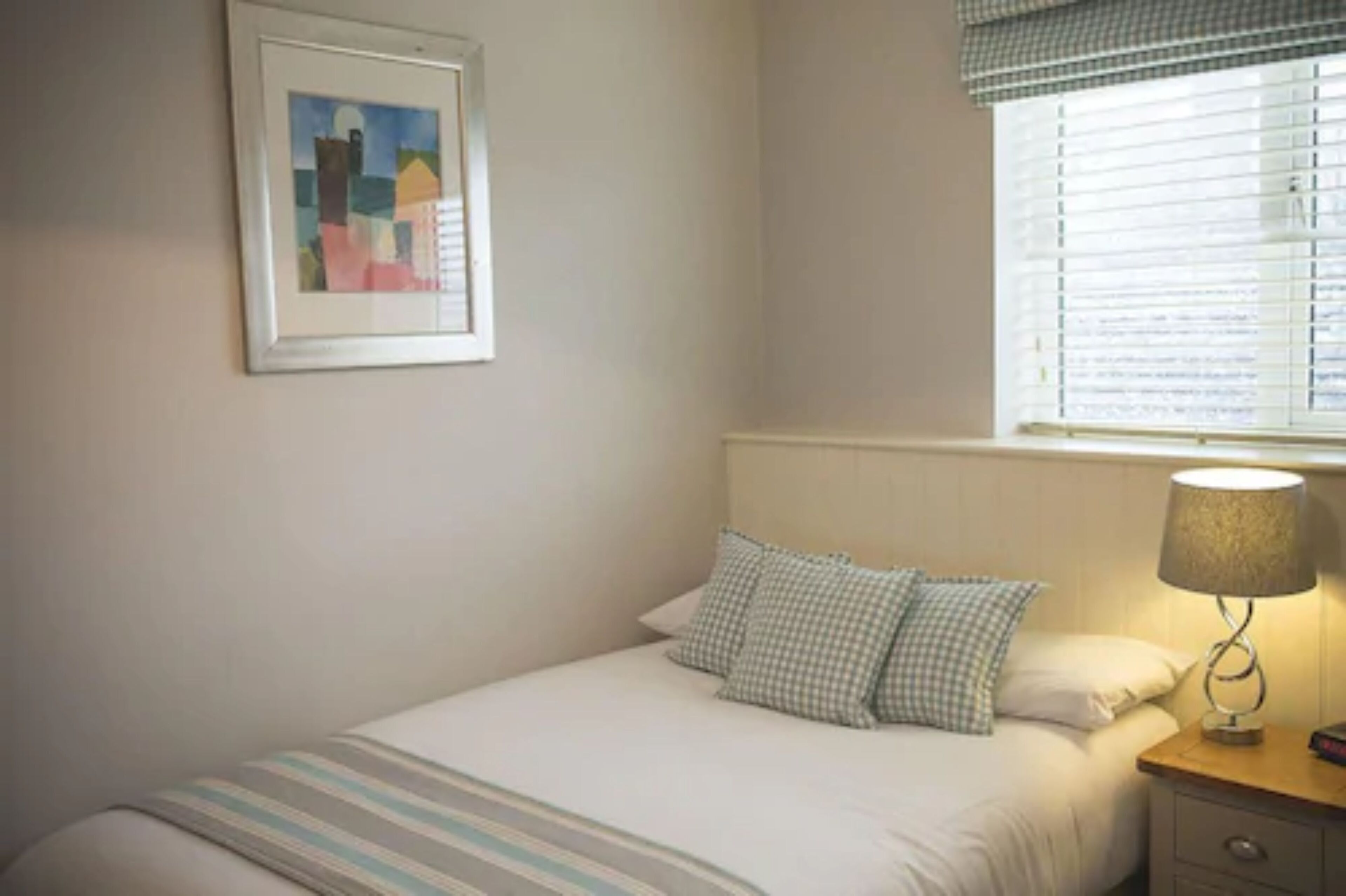 A neatly made bed with striped bedding, a checkered pillow, a bedside lamp, and a framed picture on the wall.