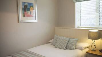 A neatly made bed with striped bedding, a checkered pillow, a bedside lamp, and a framed picture on the wall.