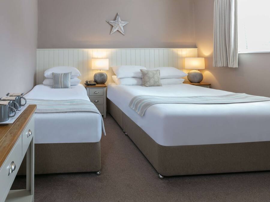 A double room with two beds, bedside tables, lamps, a star decoration on the wall, and a window with curtains.