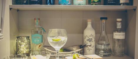 Une étagère avec différentes bouteilles de gin et un verre de gin agrémenté d’une tranche de citron vert.