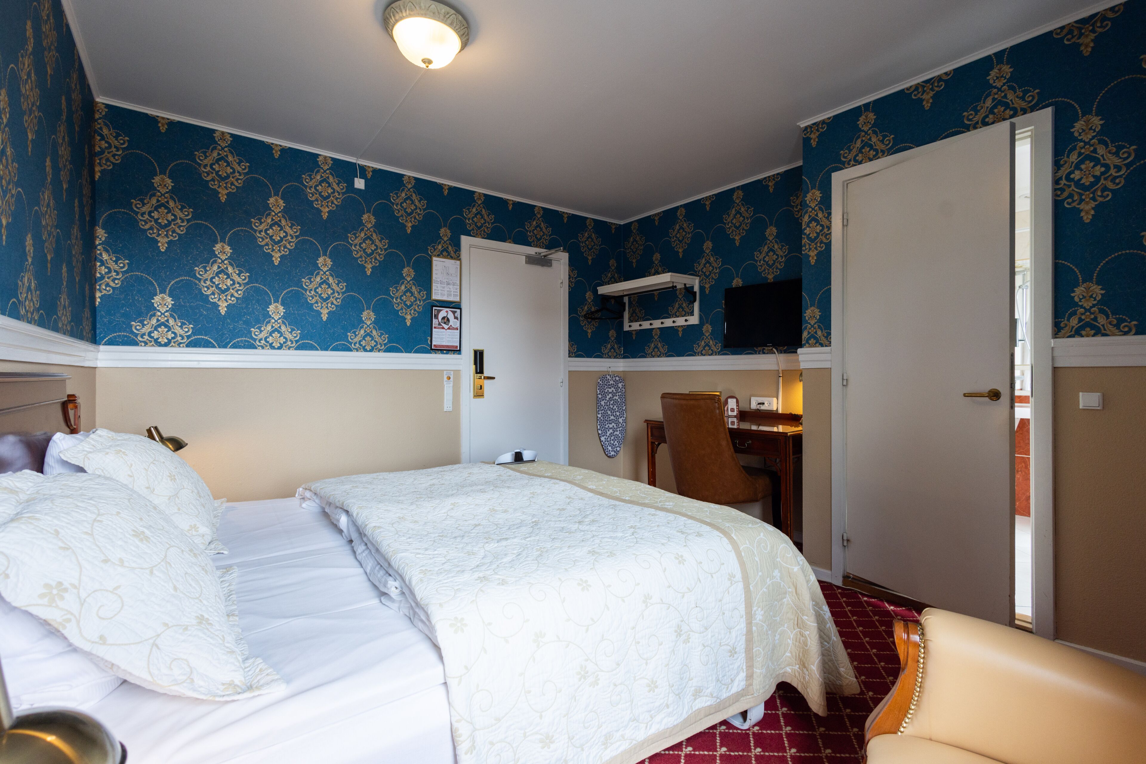 Habitación de hotel con cama doble, un escritorio con silla, televisión y puerta que da a otra habitación.