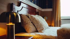 A neatly made bed with a wooden headboard, two pillows, and a bedside lamp. - Milling Hotel Plaza (Odense)