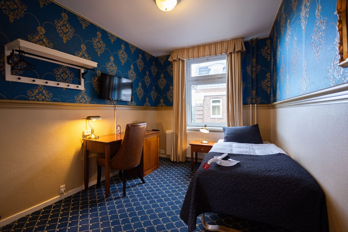 A hotel room with a bed, desk, chair, and a television mounted on the wall.