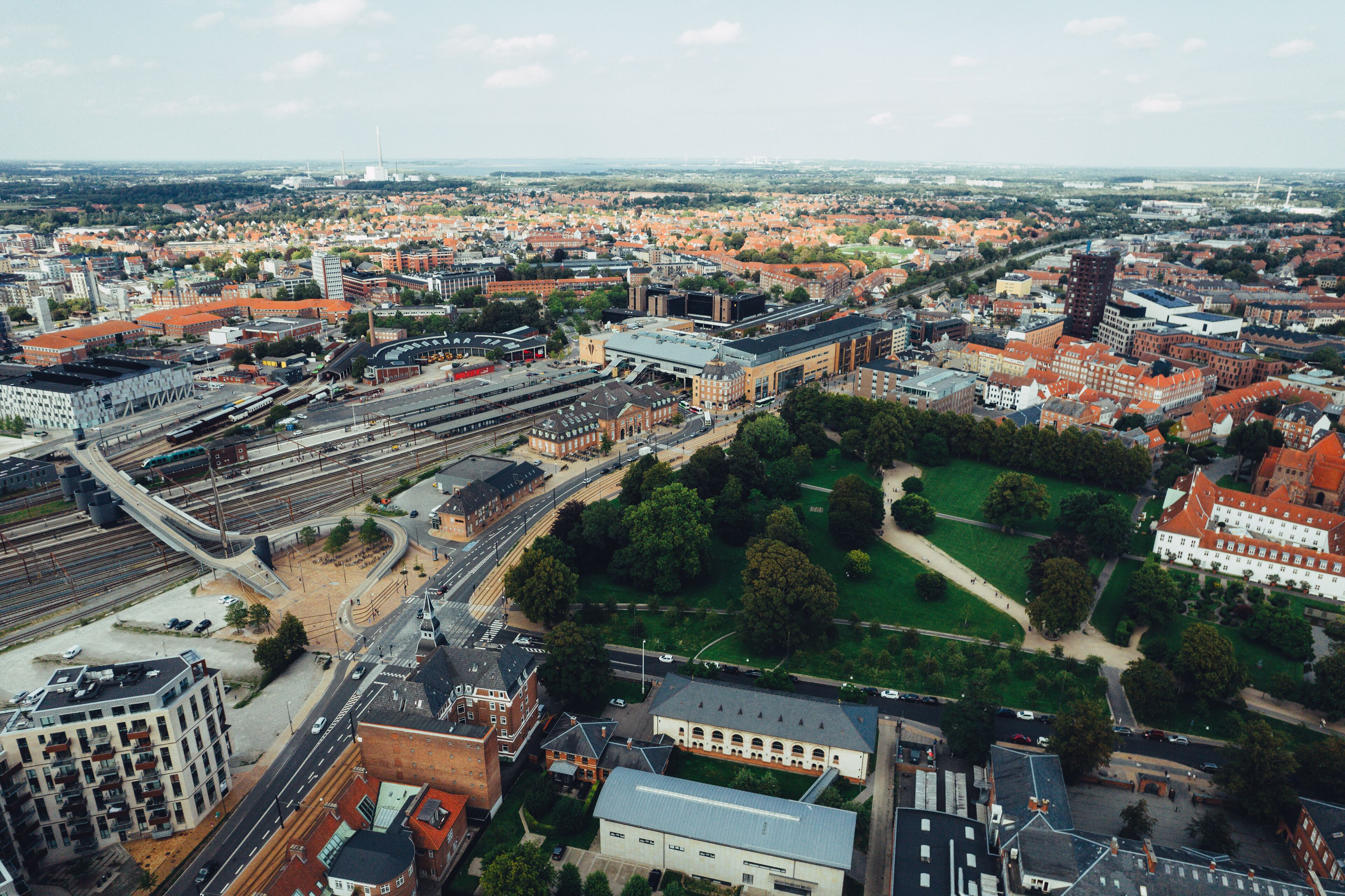 Ett flygbildsbild av en stadsbild med en blandning av bostads- och kontorsbyggnader, en järnvägsstation och grönområden.