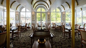 A restaurant with a high arched ceiling, large windows, and a patterned carpet. Tables are set with chairs and centerpieces. - Milling Hotel Plaza (Odense)