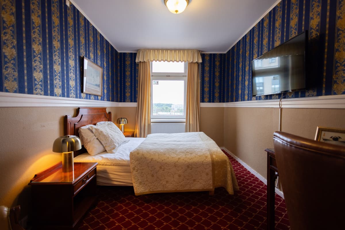 A hotel room with a bed, a nightstand, a lamp, a dresser, a television, and a window with curtains.