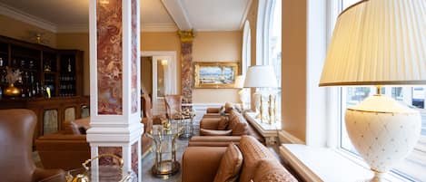 Un salon luxueux avec un canapé, des fauteuils, une table basse en verre et une lampe.