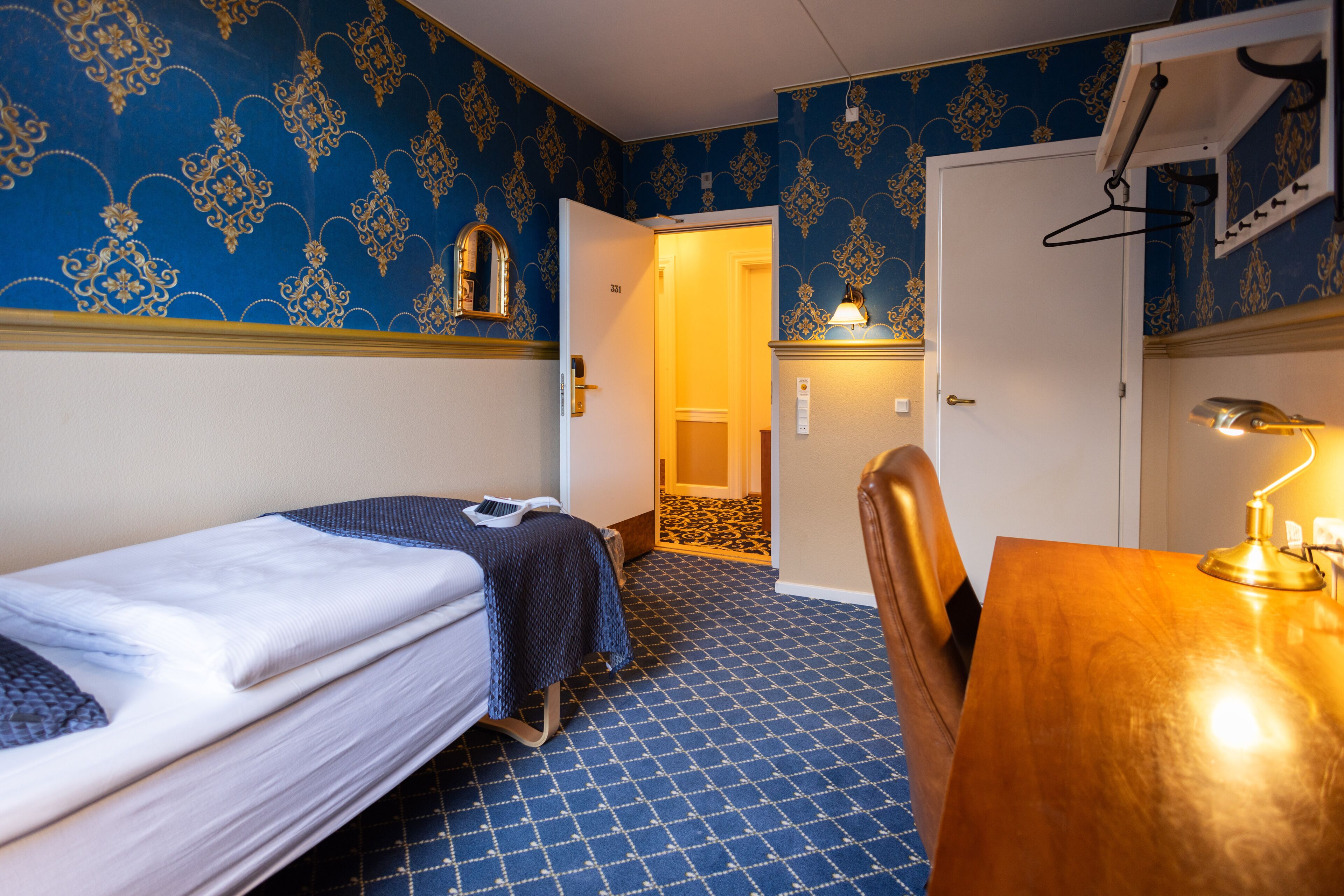 A room with a bed, a desk, a chair, and a door leading to another room.