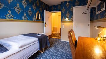 A room with a bed, a desk, a chair, and a door leading to another room.