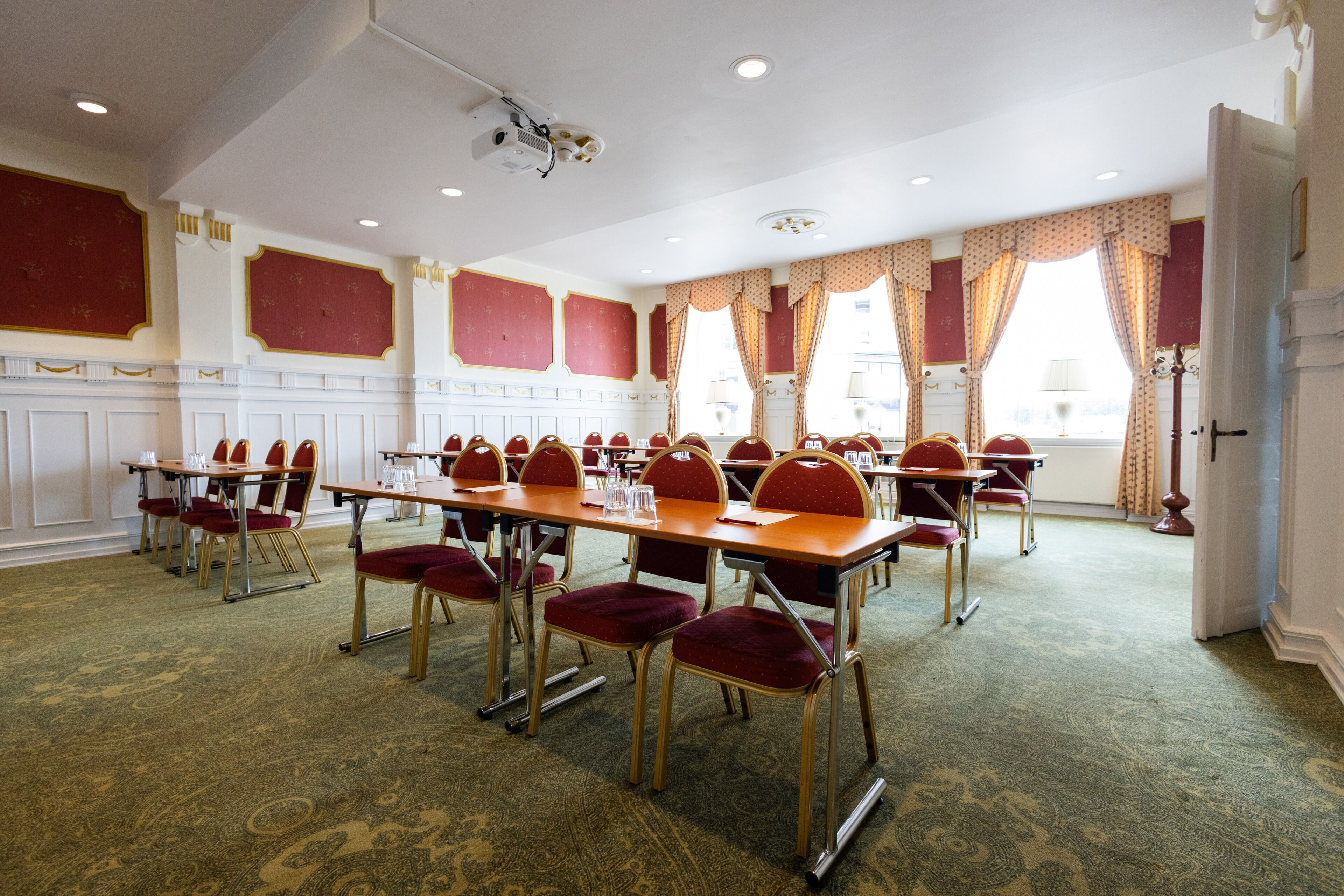 A conference room with multiple tables and chairs, a projector, and large windows with curtains.