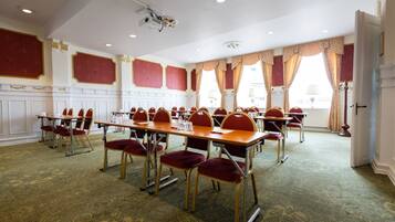 A conference room with multiple tables and chairs, a projector, and large windows with curtains.