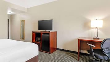 A hotel room with a bed, a desk with a chair, a television, and a lamp.