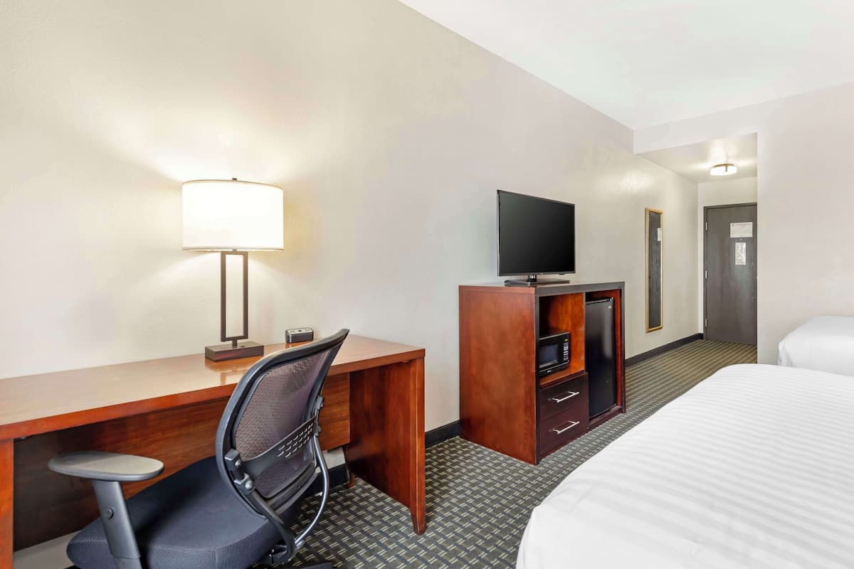 A hotel room with a bed, a desk with a chair, a television, and a minibar.