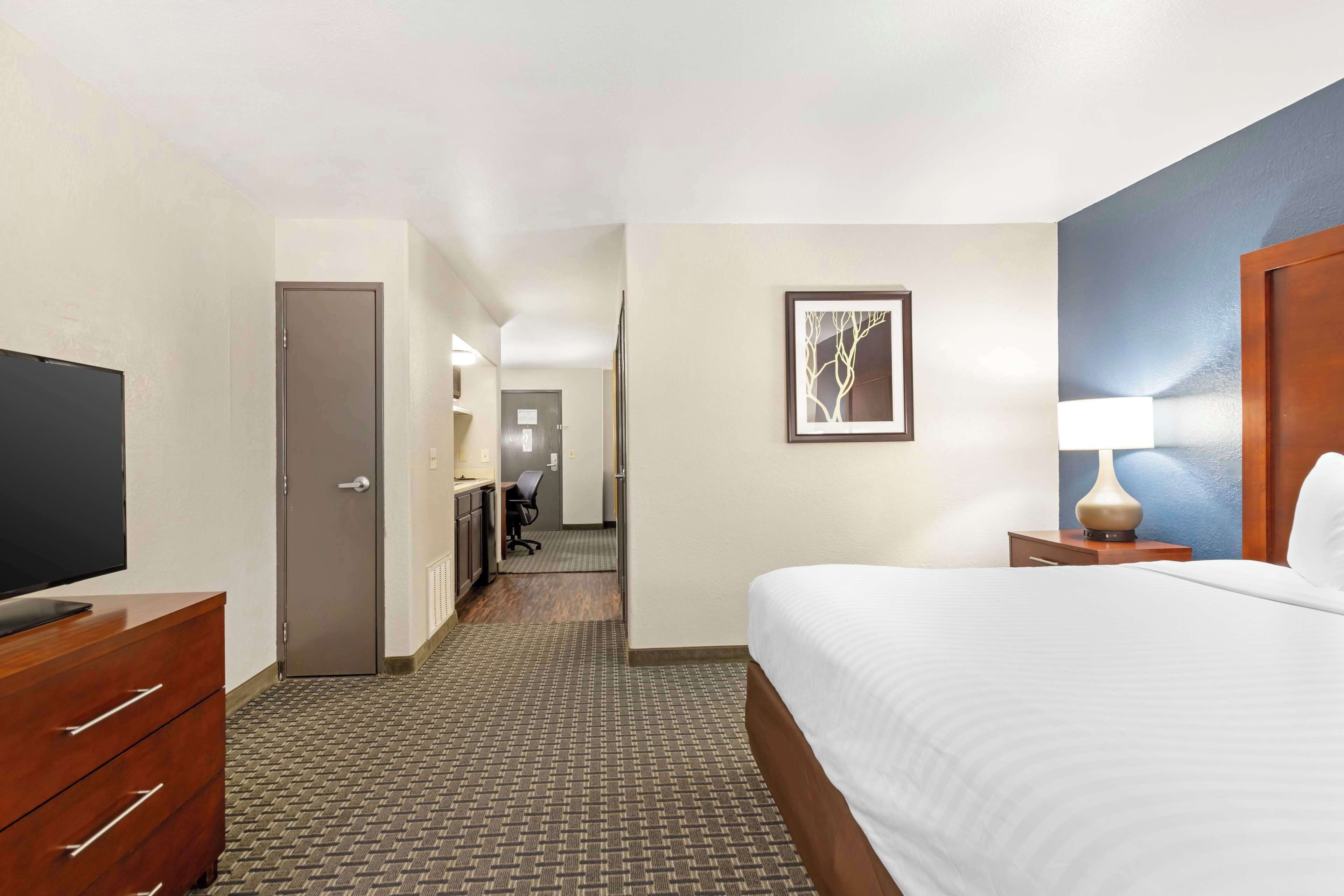 A hotel room with a large bed, a television on a wooden dresser, a desk with a chair, and a painting on the wall.