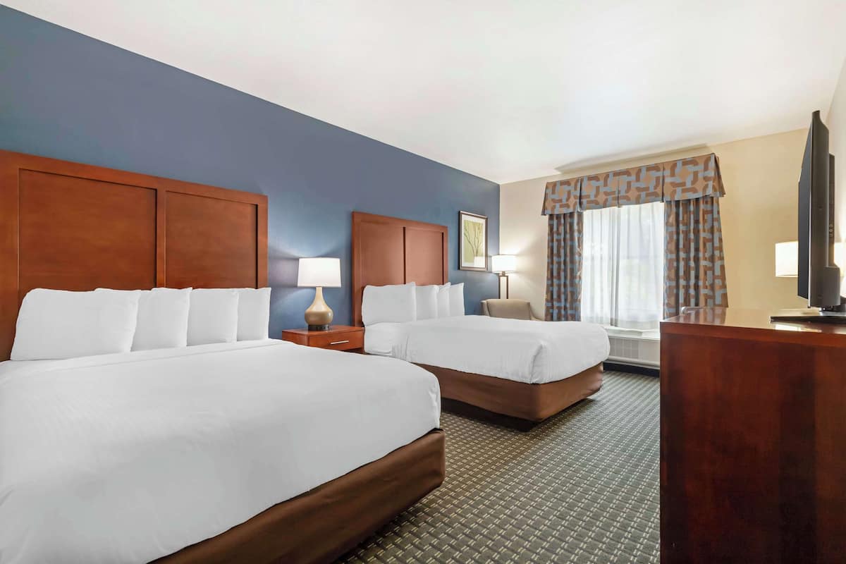 A hotel room with two beds, a desk, a TV, and a window with curtains.