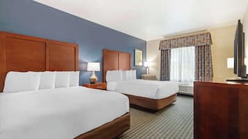 A hotel room with two beds, a desk, a TV, and a window with curtains.