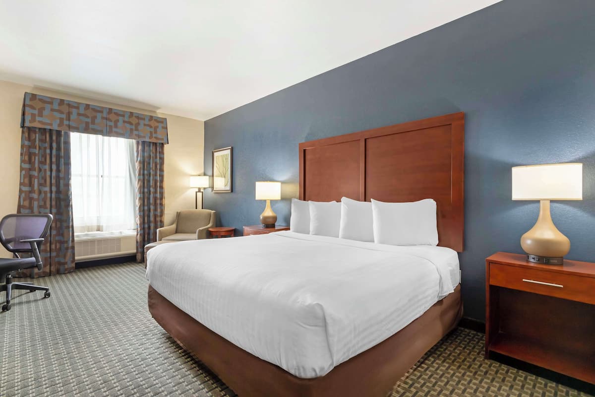 A hotel room with a large bed, a desk, a chair, a lamp, and a window with curtains.