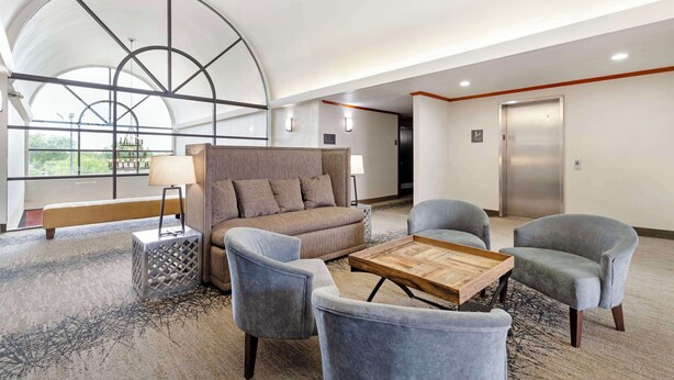 A spacious lobby with a large arched window, a sofa, two armchairs, a coffee table, and an elevator.