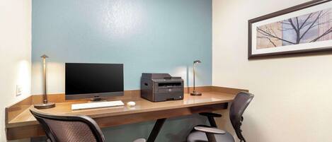A hotel room with a wooden desk, two office chairs, a flat-screen TV, a printer, and two desk lamps.