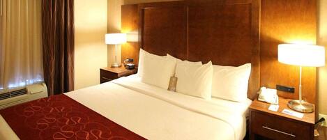 A hotel room with a large bed, two bedside tables, a wooden headboard, a red patterned bedspread, and two lamps.