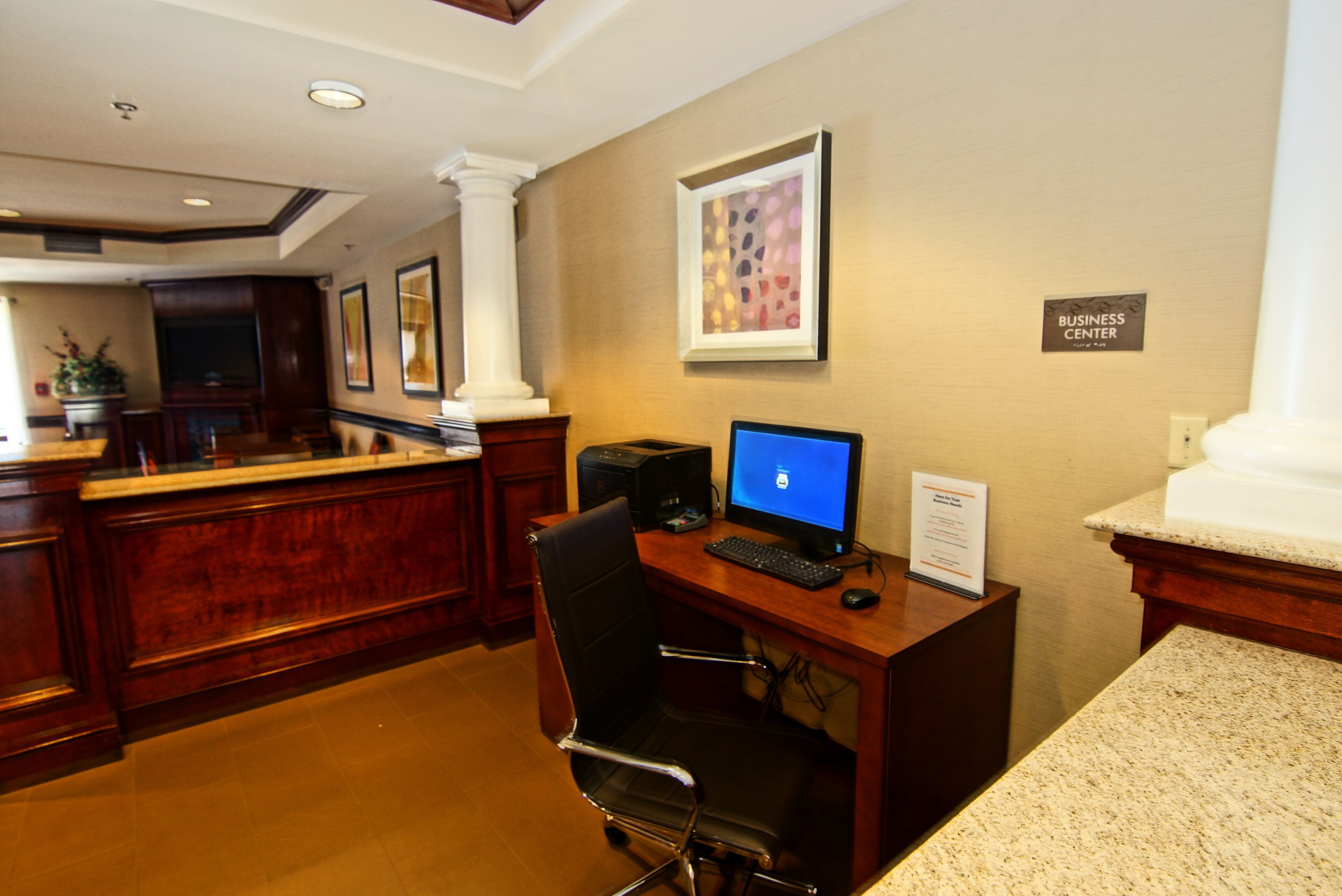 A reception desk with a computer, a chair, and a framed artwork on the wall.