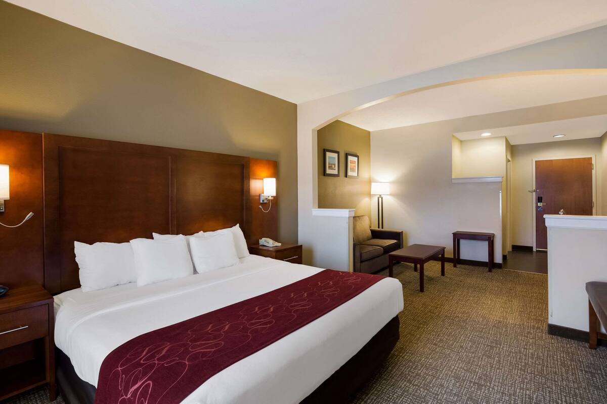A hotel room with a large bed, a desk, a chair, and a small table.