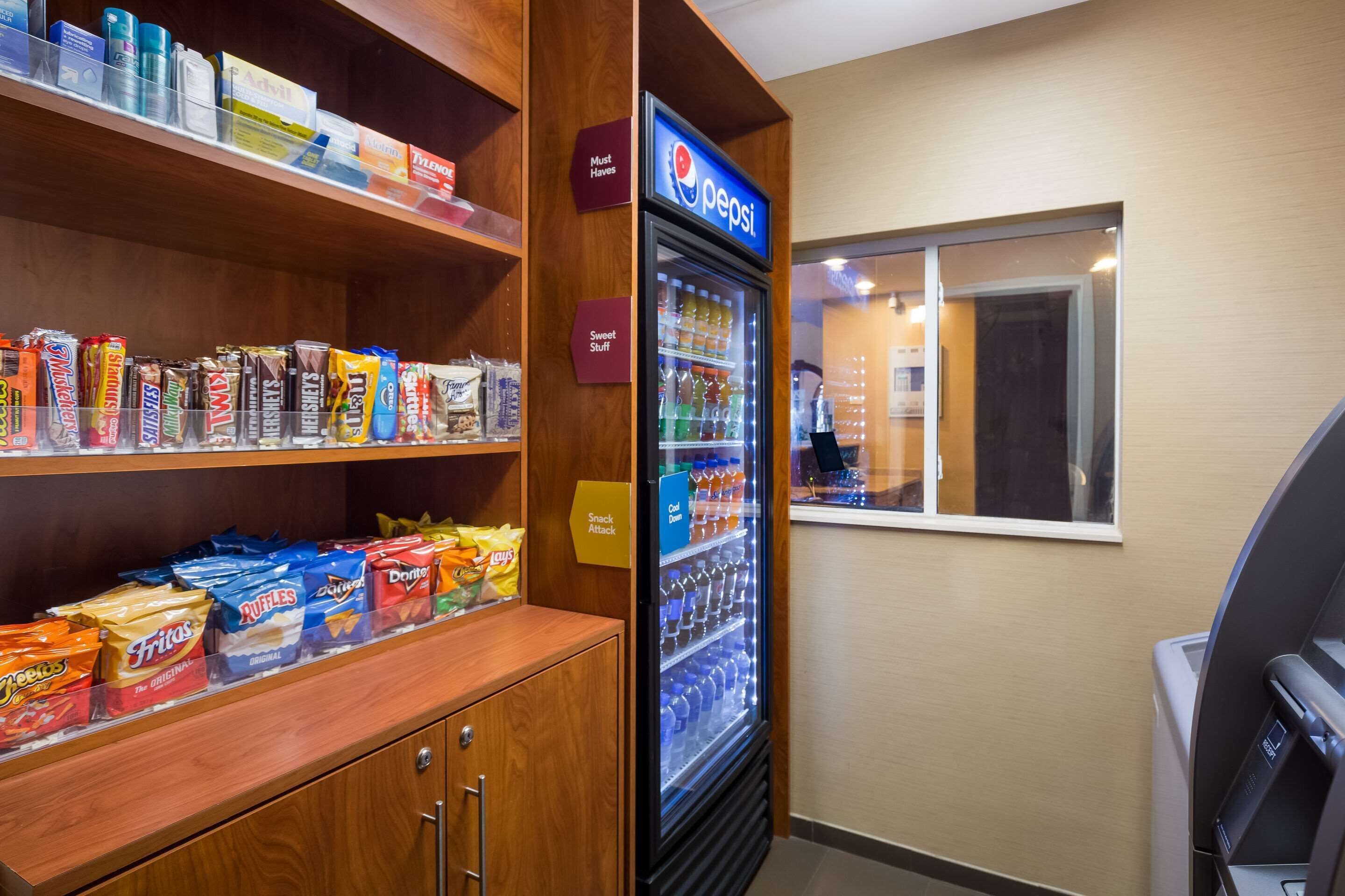 A snack display with various chips and candies, a Pepsi refrigerator, and a window with a view of the interior.