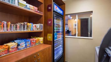 A snack display with various chips and candies, a Pepsi refrigerator, and a window with a view of the interior.