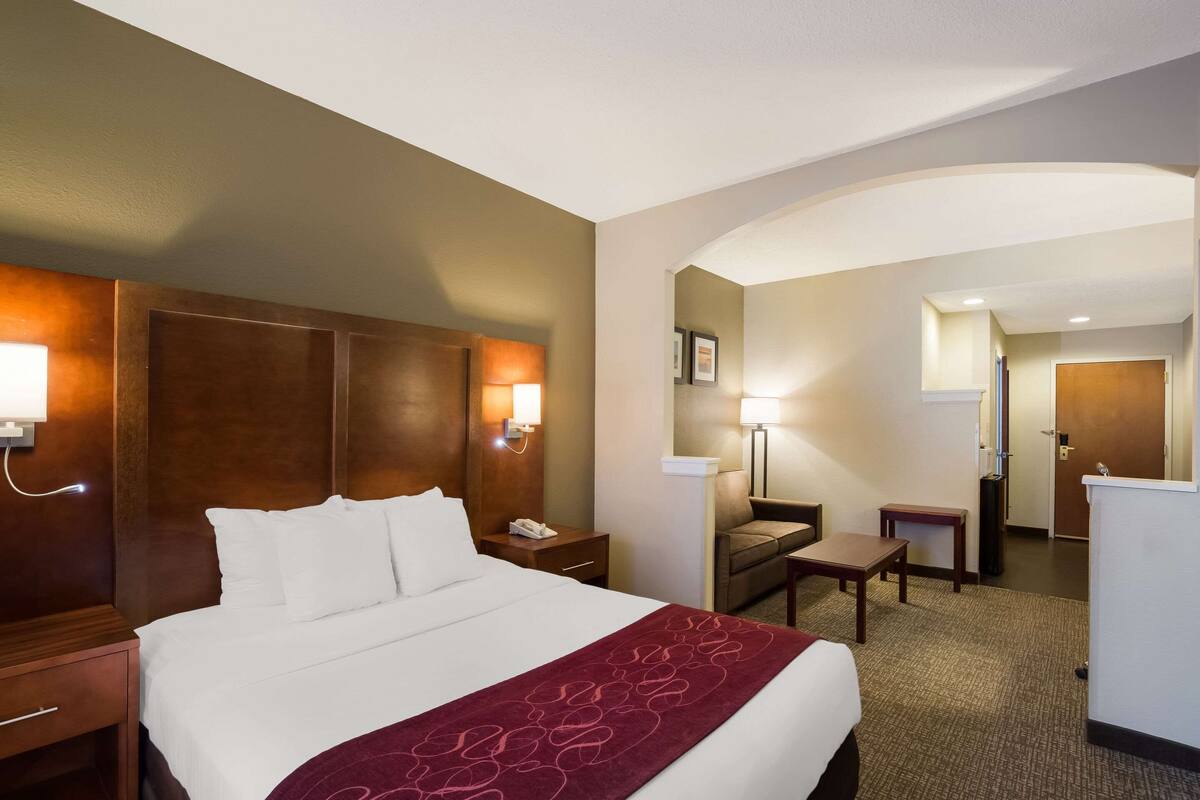 A hotel room with a large bed, a desk, a chair, and a desk lamp.