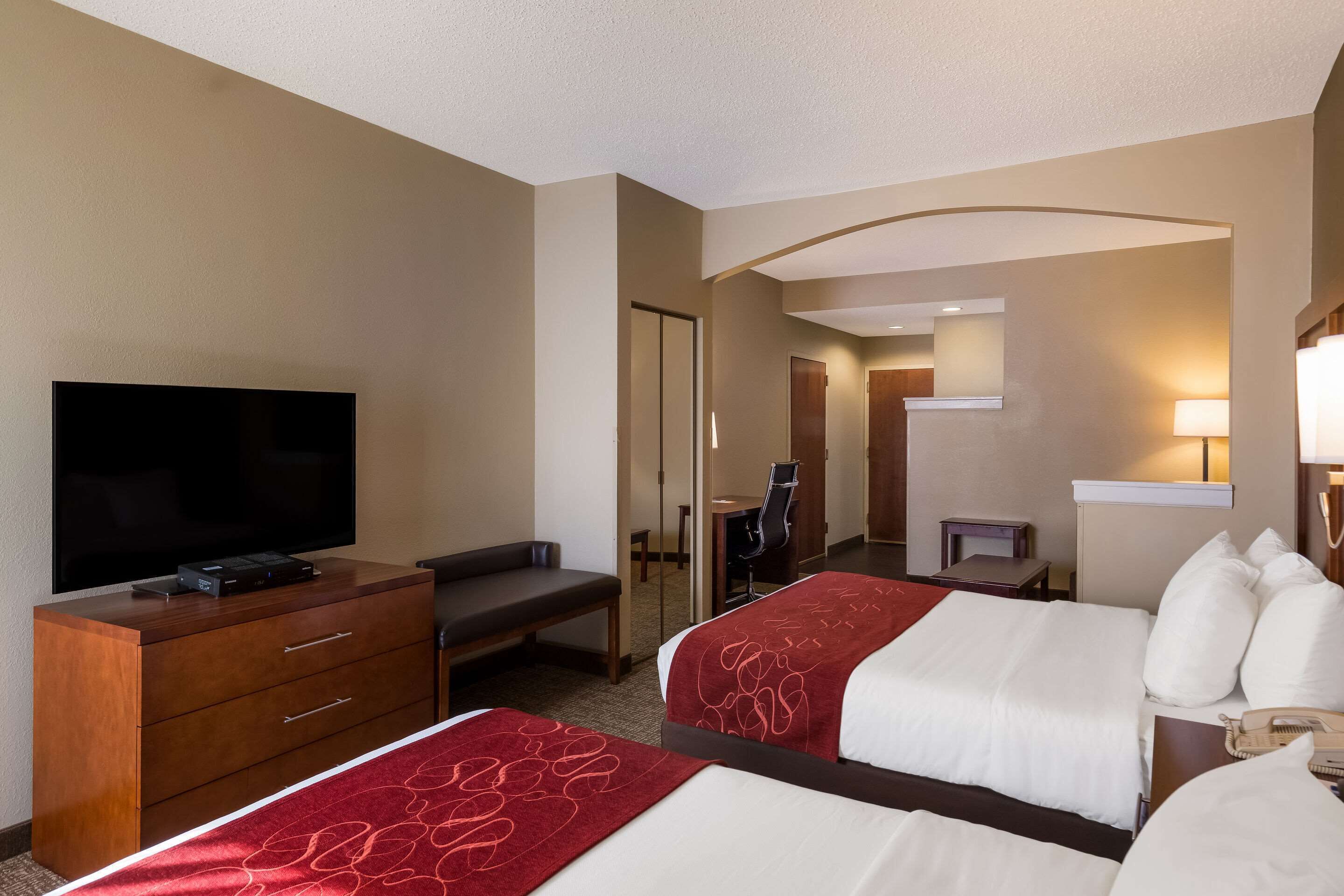 Ein Hotelzimmer mit zwei Betten, einem Fernseher, einem Schreibtisch und einem Spiegel.