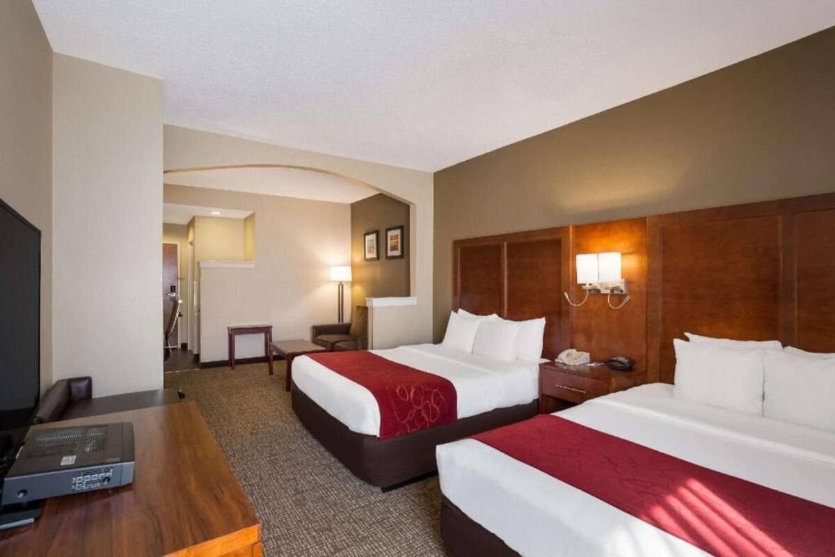 A hotel room with two beds, a desk with a projector, a TV, and a lamp.