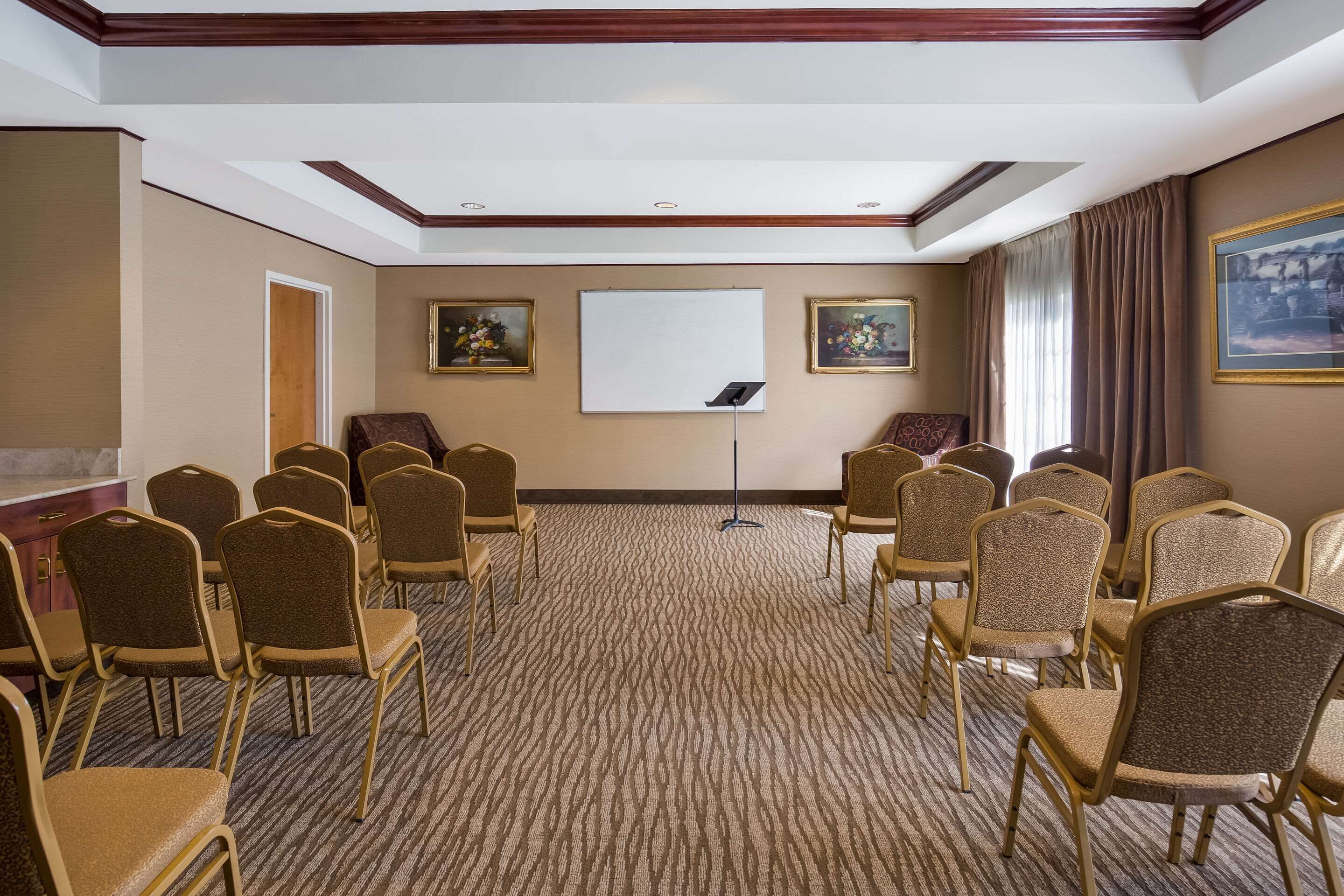 Uma sala de conferências com fileiras de cadeiras, um quadro branco e duas imagens emolduradas nas paredes.