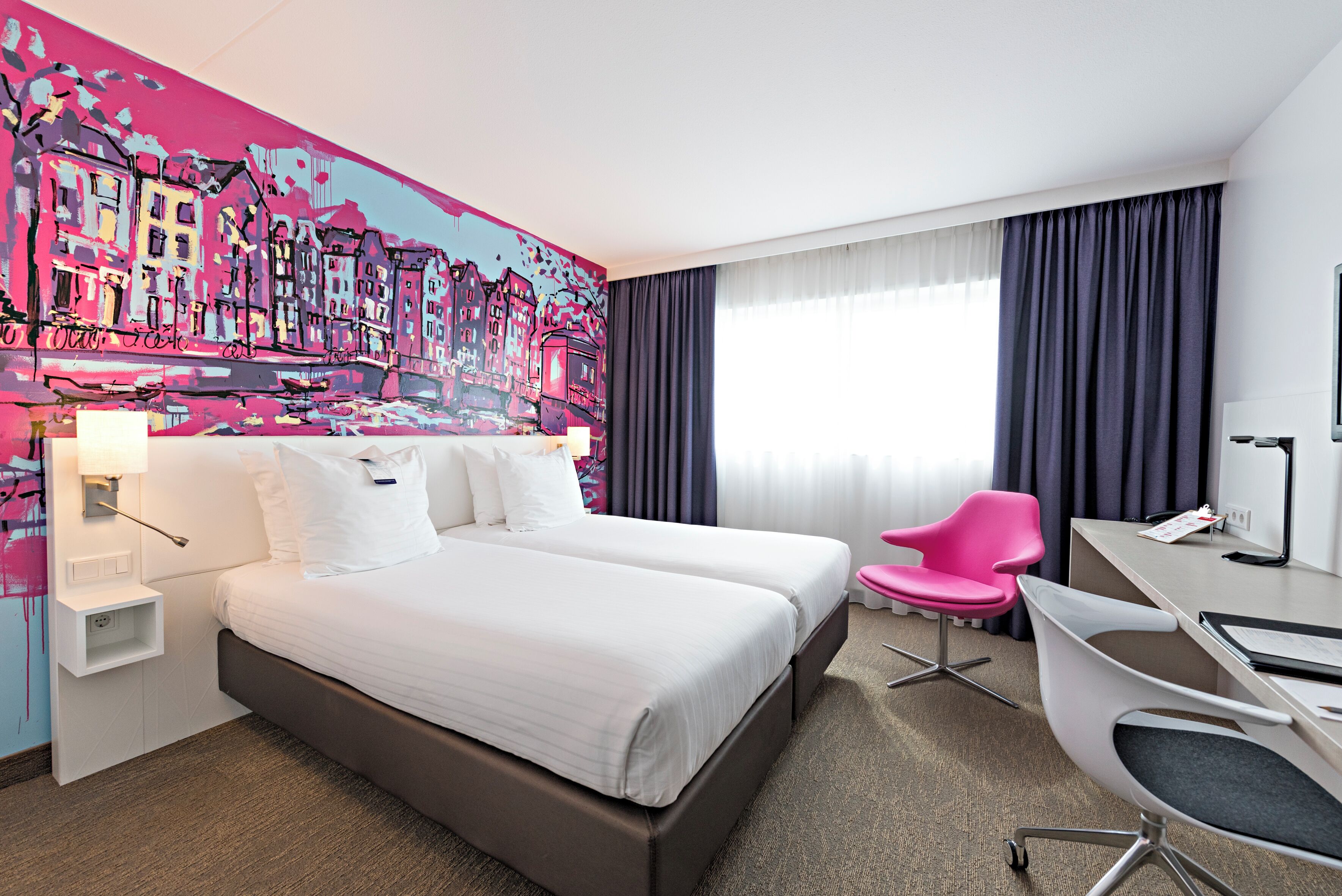 A hotel room with a large bed, a desk, a chair, and a colorful mural on the wall.