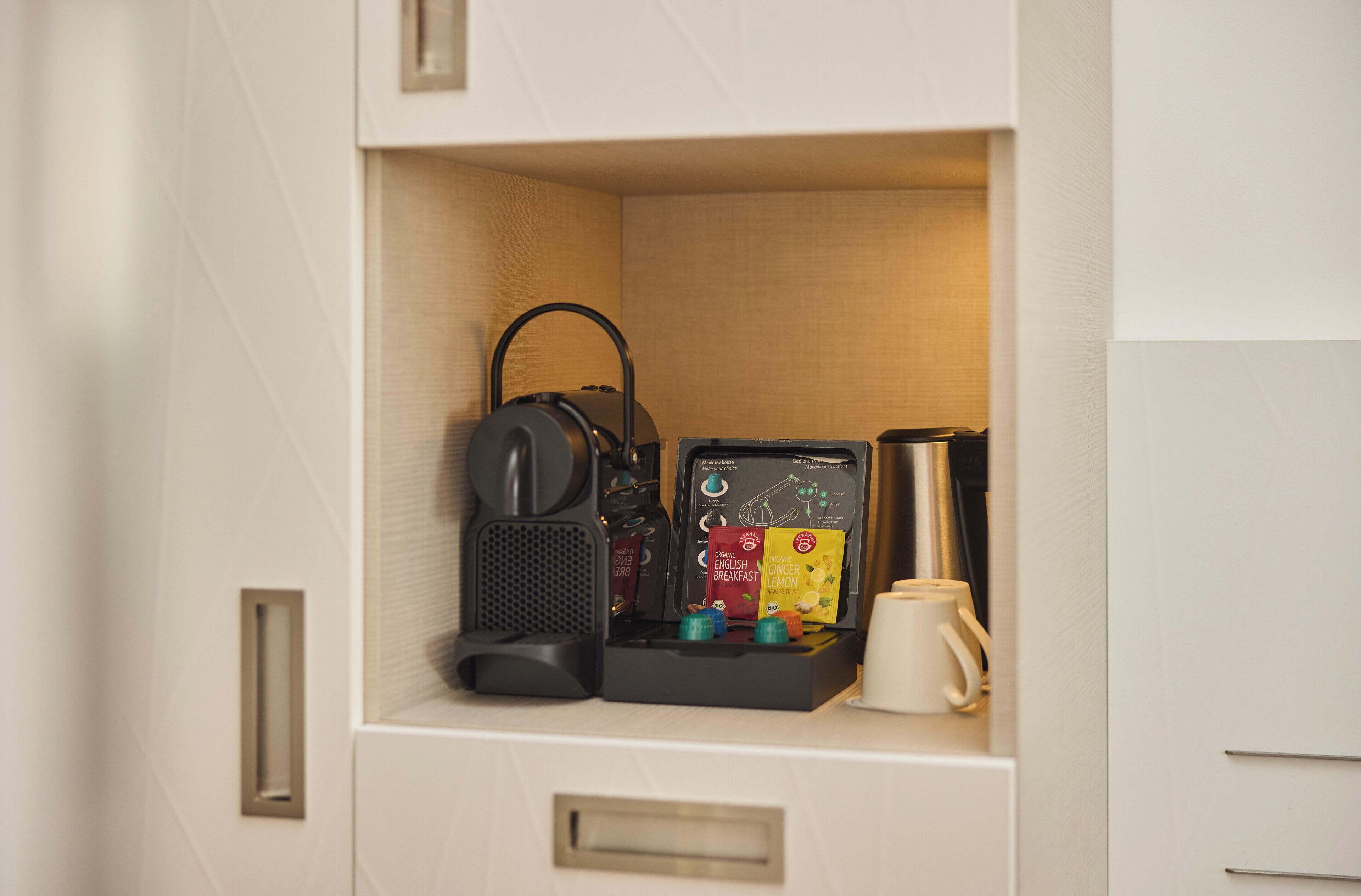 A compact kitchenette with a coffee maker, tea bags, and a coffee pot.