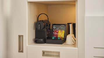 A compact kitchenette with a coffee maker, tea bags, and a coffee pot.