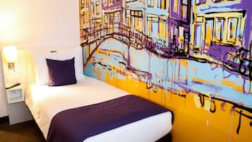 A hotel room with a bed, a nightstand, a lamp, and a large colorful mural on the wall.