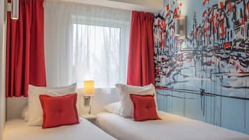 Habitación de hotel con dos camas, ropa de cama roja y blanca, una ventana con cortinas traslúcidas y una pared con arte abstracto.