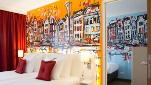 Een hotelkamer met een groot bed, rode gordijnen, een witte nachtkastje en een stadsgezichtschilderij aan de muur.