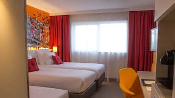 A hotel room with two beds, a desk with a chair, a television, and a large window with curtains.