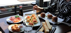 Una mesa de comedor con diversos alimentos, una copa de vino tinto y una botella de salsa.