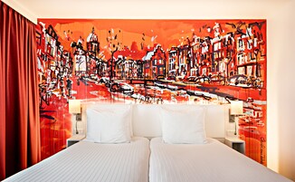 Ein Hotelzimmer mit einem großen, abstrakten Gemälde an der Wand, einem Bett mit weißen Bettwäsche und einem roten Vorhang.