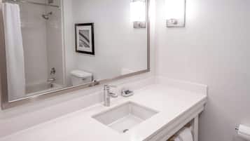 Un baño moderno con un lavamanos blanco, un espejo grande y una zona de ducha.
